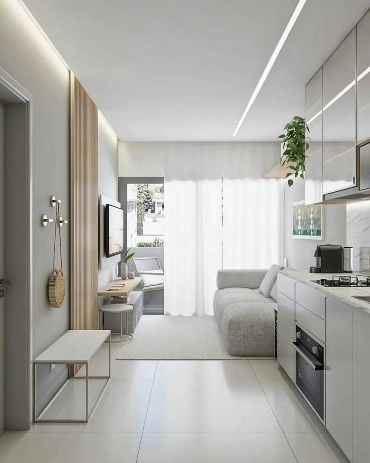 foto de cozinha e sala integrados em apartamento pequeno em tons claros, com brancos, espaço para pendurar bolsas, janela grande, TV em painel, sofá cinza e mais. 