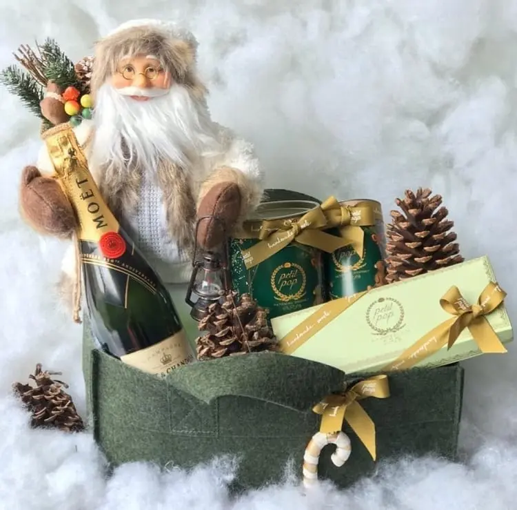 cesta feita de feltro verde com Papai Noel, latas, pinhão, champanhe e doce