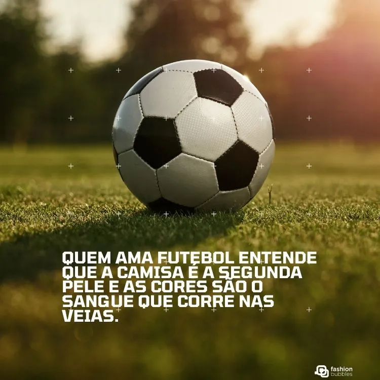 Uma clássica bola de futebol branca e preta repousa sobre a grama verde de um campo, iluminada pelo sol. O texto em português afirma: "Quem ama futebol entende que a camisa é a segunda pele e as cores são o sangue que corre nas veias." A cena transmite a conexão íntima e a lealdade dos fãs ao esporte.