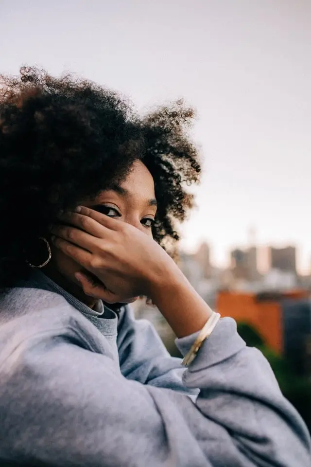 Mulher de pele negra usando blusa cinza com uma mão no rosto
