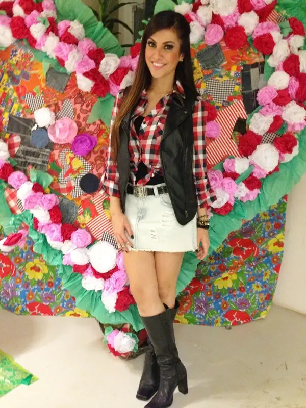 Mulher usando camisa xadrez + colete de couro + saia jeans + bota cano médio