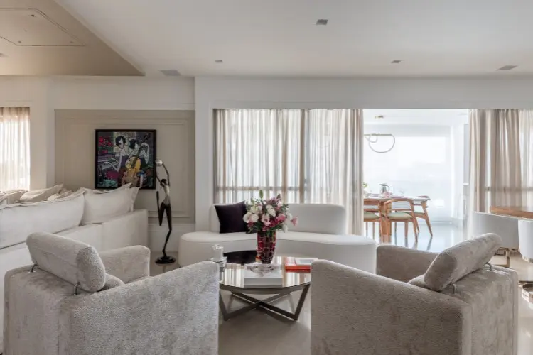 Sala de estar com janela grande, quadros, poltronas, mesa de centro com vaso de flores 