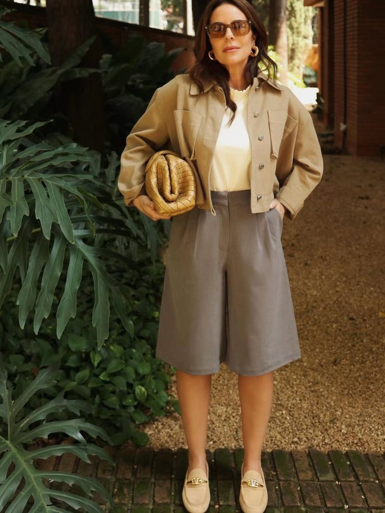 Mulher de pele clara usand blusa branca, jaqueta cropped creme, bermuda de alfaiataria cinza e mocassim de camurça bege