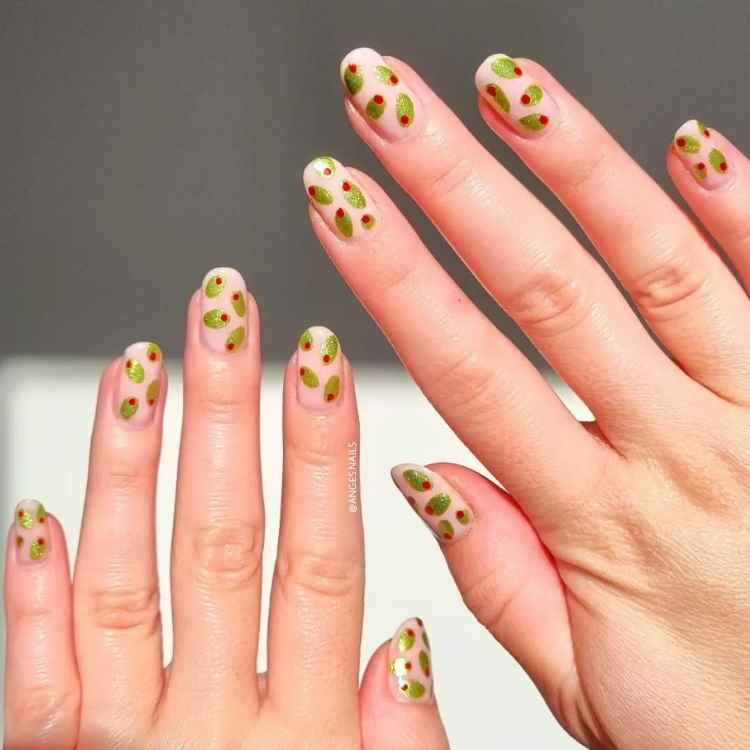 Unhas curtas com esmalte nude decorado com manchas verdes e pontos vermelhos metálicos, remetendo a um estilo moderno e ousado. As mãos estão abertas contra um fundo claro, destacando o contraste das cores vibrantes e o acabamento brilhante do design.