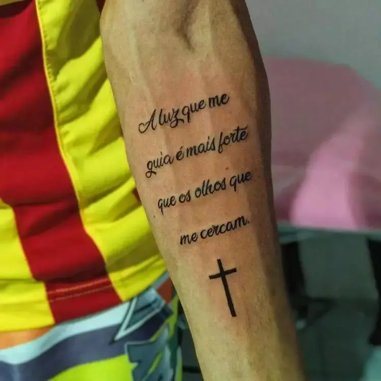 tatuagem escrita A luz que me guia é mais forte que os olhos que me cercam no braço