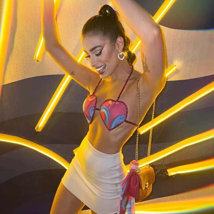 Mulher de pele clara com abadá personalizado em top de coração, além de uma saia bege 