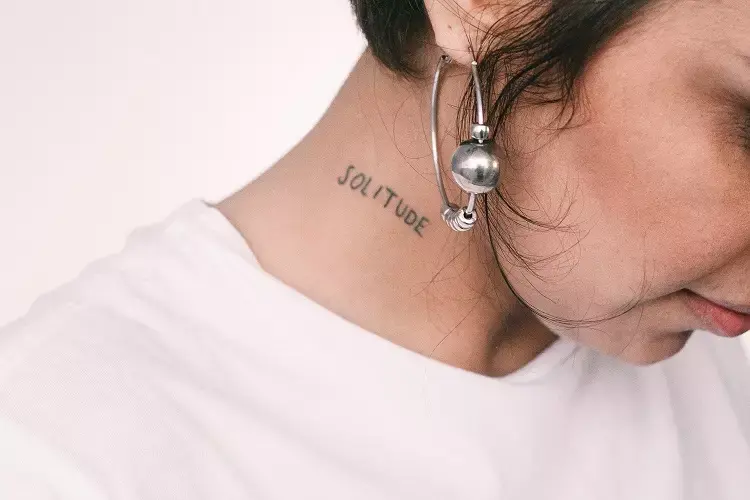 palavra solitude tatuada no pescoço