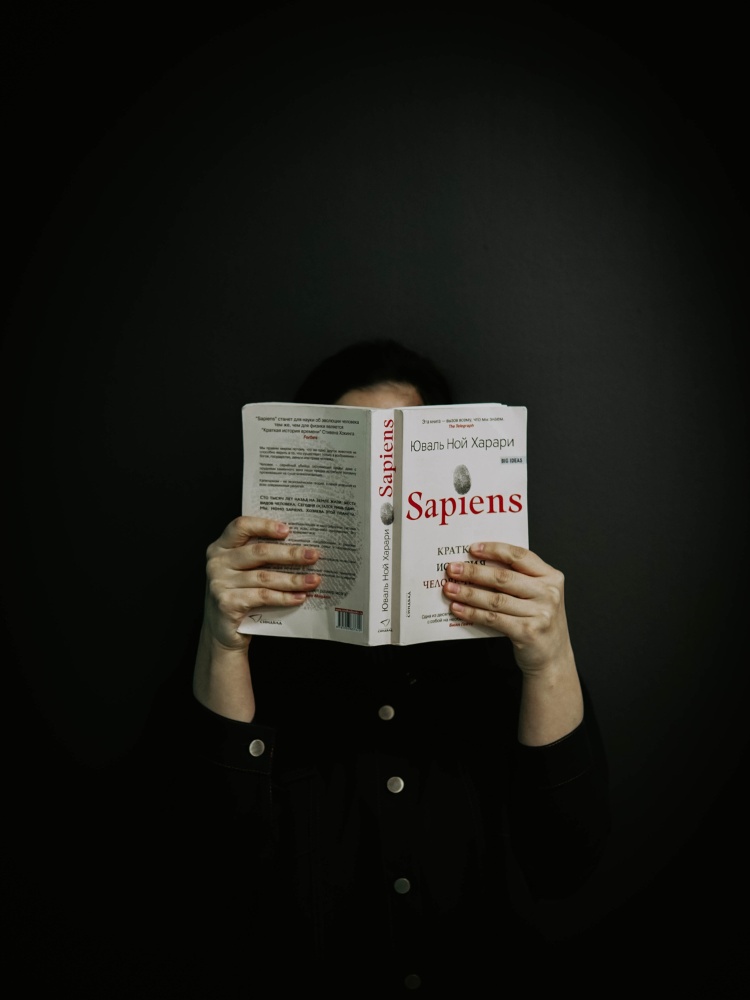 Pessoa de pele clara com roupa preta lendo livro "Sapiens"