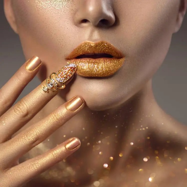 Mulher de pele clara com batom dourado e unhas douradas