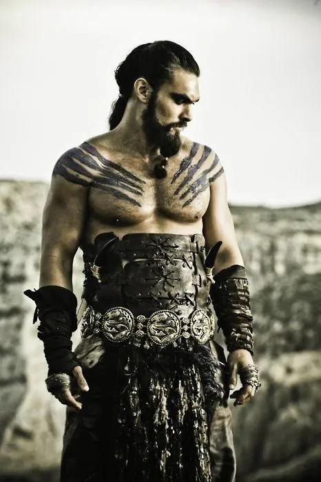 Jason Momoa com tinta preta nos ombros, cabelo longo e armadura 