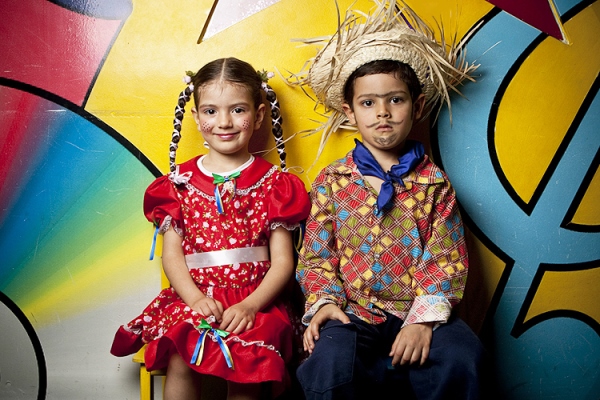 Menino e menina com trajes juninos: vestido vermelho e camisa xadrez colorida com calça jeans