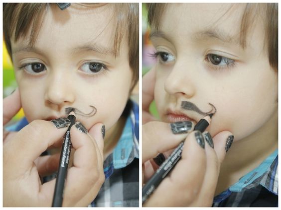 Mãe fazendo bigode com lápis preto no rosto de filho 