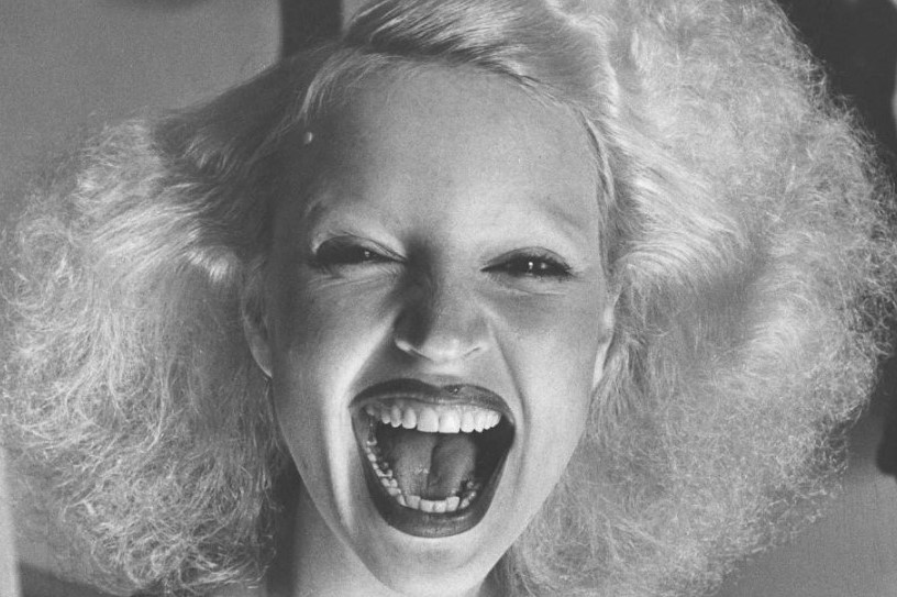 Foto em preto e branco do rosto de Elke Maravilha jovem sorrindo de boca aberta. Retrato em preto e branco de Elke Maravilha jovem sorrindo de boca aberta.