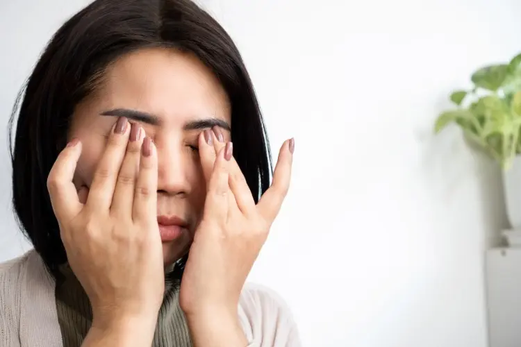 Mulher de pele clara com roupa cinza e mãos nos olhos 