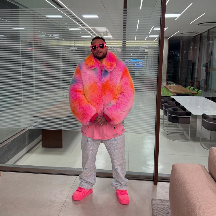 Neymar Jr. posa em um casaco de pele colorido, óculos de sol rosa e calça Louis Vuitton. Com a recente notícia de uma proposta de salário do Fenerbahçe, o jogador exibe um estilo ousado em um ambiente moderno de escritório.

