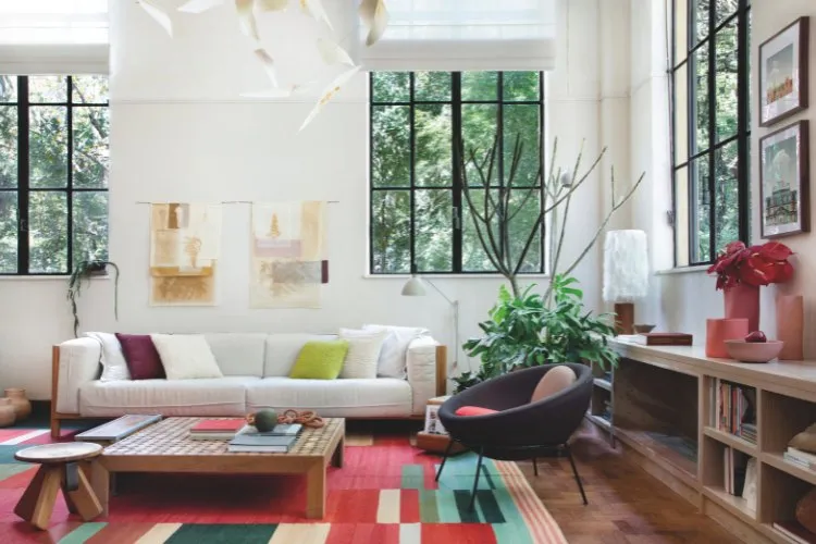 Sala com tapete colorido, grandes janelas, sofá claro, poltrona roxa, mesa de centro e mais 