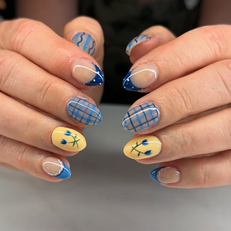 Unhas arredondadas com nails artes em azul, como francesinha e xadrez, além de unha amarela com flor azul