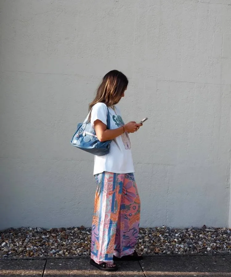 uma mulher usando uma camiseta branca, uma calça estampada e uma bolsa azul