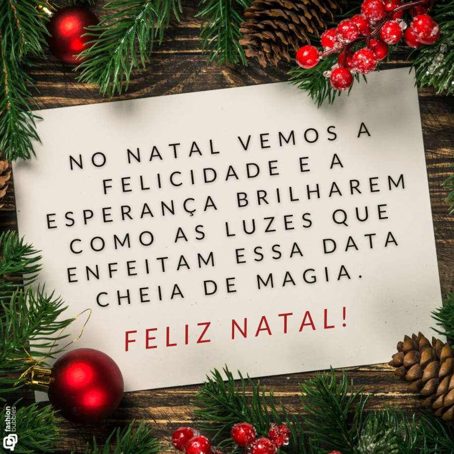 Mesa de madeira com enfeites natalinos e papel com frase: No Natal vemos a felicidade e a esperança brilharem como as luzes que enfeitam essa data cheia de magia. Feliz Natal!