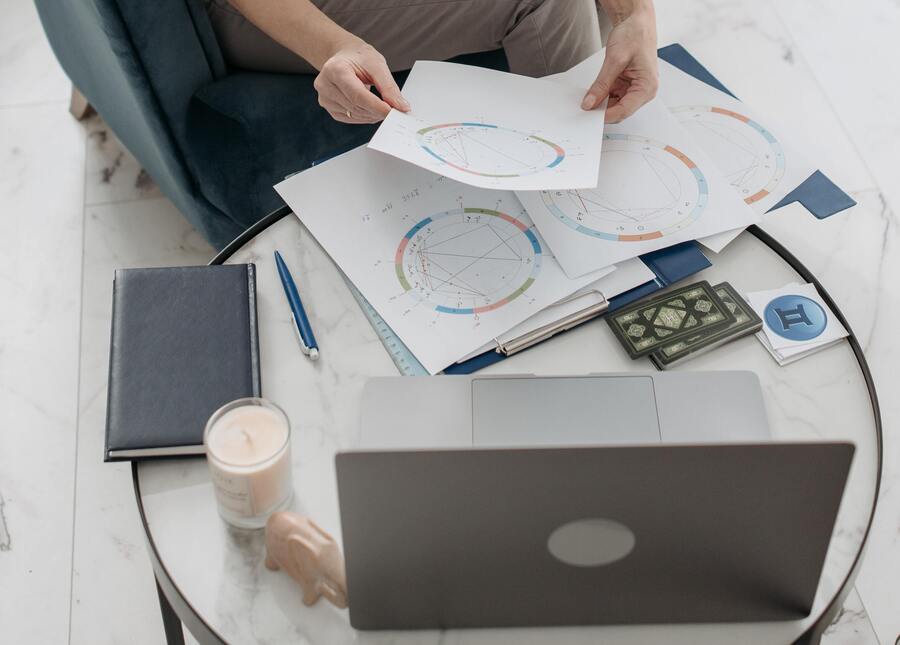 uma mulher mexendo em papéis sobre mapas astrais em uma mesa com um notebook