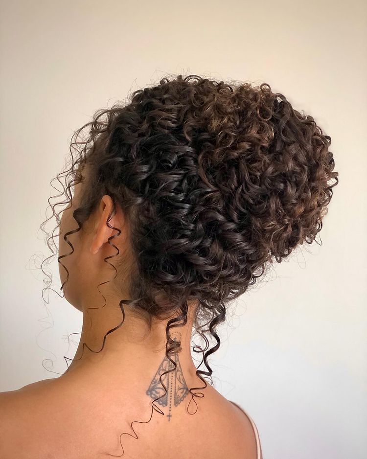 Cabelo cacheado castanho escuro preso em coque.
