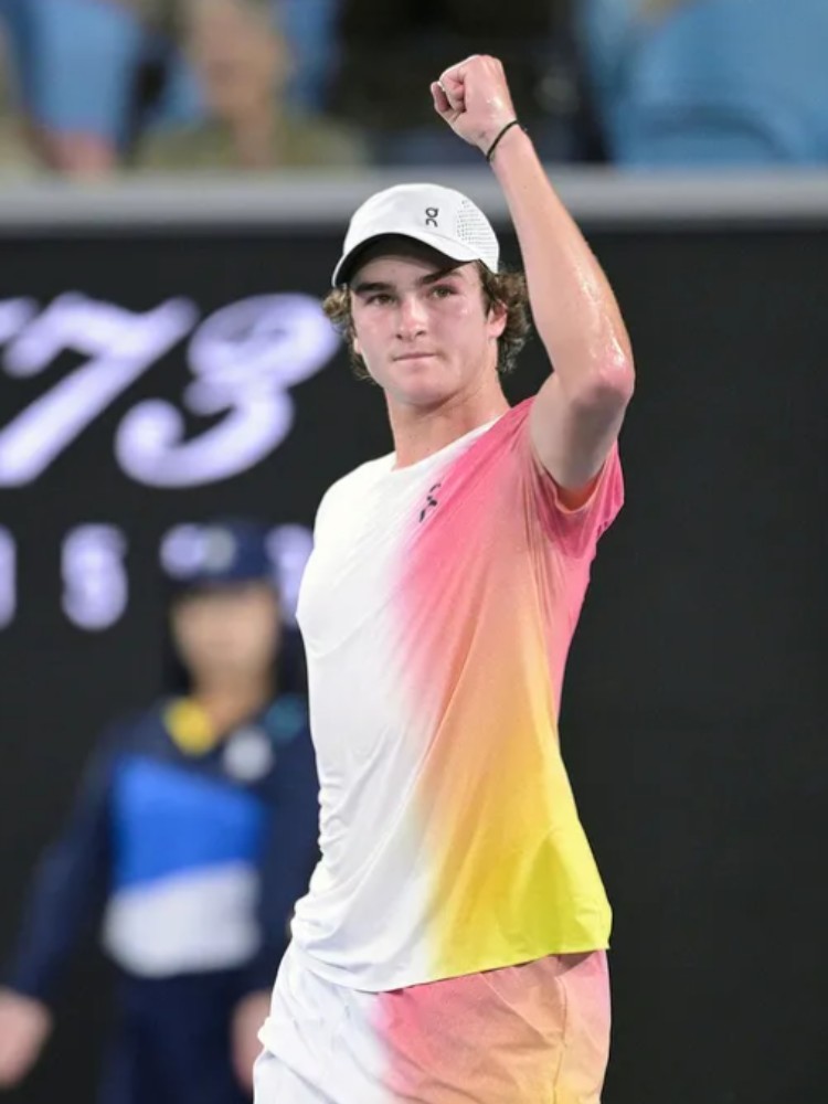 João Fonseca em quadra usando boné branco e blusa branca com degradê rosa e amarelo