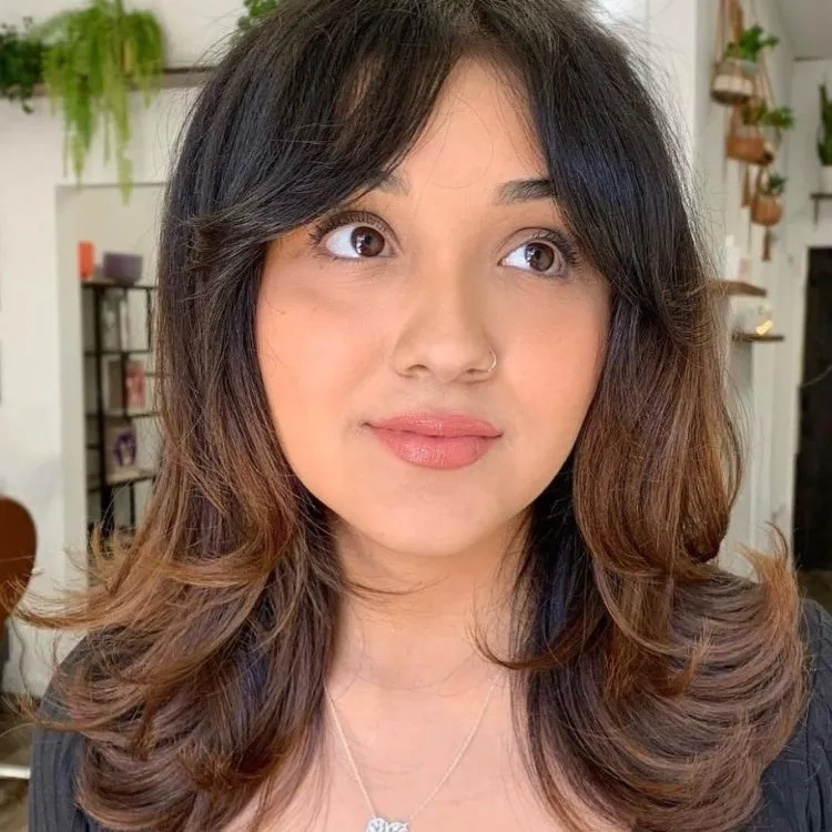 Uma mulher branca de cabelos e olhos castanhos com um corte de cabelo repicado um pouco abaixo dos ombros
