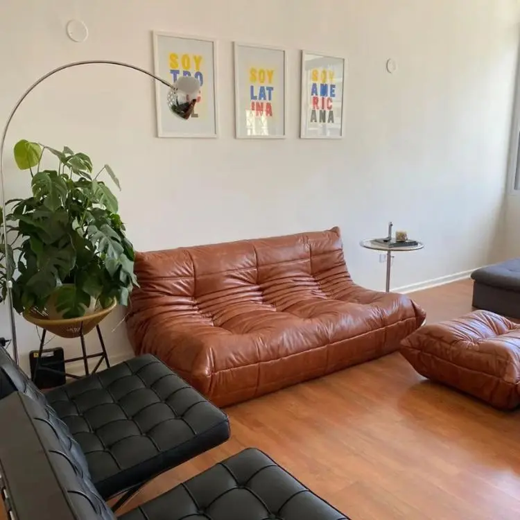 Sala de piso de madeira com duas poltronas de couro pretas e um puff marrom em couro sintético