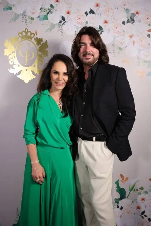 Cris Porto de verde e Stephane Rolland de terno preto e calça off-white em fundo com papel de parede com logo da Cris Porto joalheria e flores