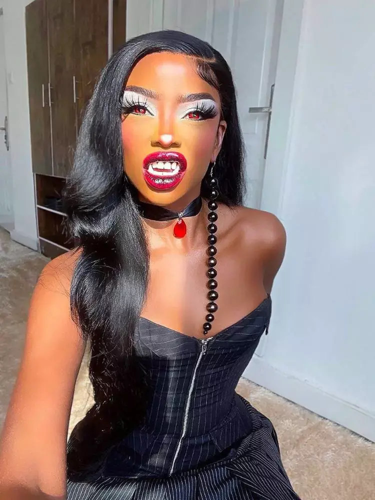 Mulher de pele negra usando corset preto, sombra clara esfumada, cílios postiços, batom vinho e dentadura de vampiro