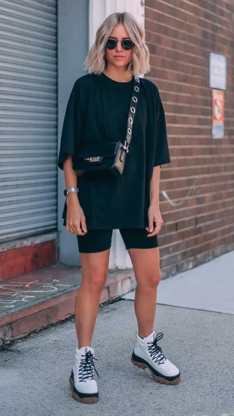 Mulher de pele clara usando camiseta preta, shorts biker preto e coturno branco