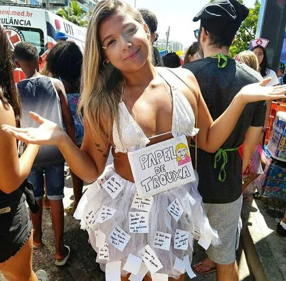 Foto de mulher de pele clara com look branco, plaquinha "papel de trouxa" e post-its na saia com frases 