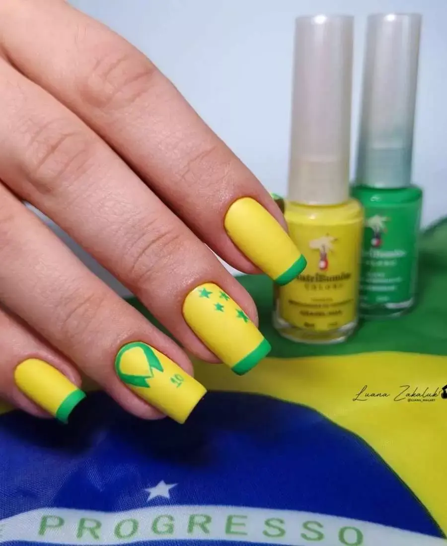 Imagem de mão com unhas decoradas de Brasil. Cores usadas, verde e amarelo. Polegar: amarelo com francesinha verde. Indicador: amarelo com francesinha verde. Dedo Médio, amarelo com francesinha verde e estrelinhas. Anelar: amarelo com desenho de camisa 10. Mínimo: amarelo com francesinha verde.