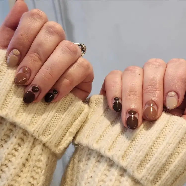 Mãos de pele clara com nails arts redondas em degradê de marrom escuro ao bege 