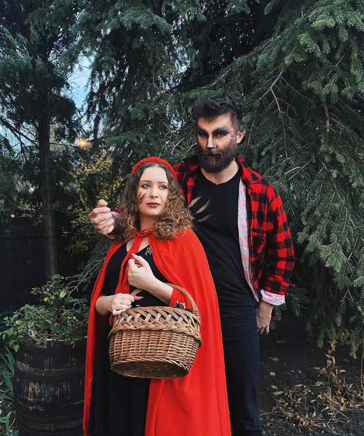 Fantasia de casal para o Halloween: Chapeuzinho vermelho e o lobo mau. Ela usa tiara vermelha, capa vermelha, machucado falso no rosto e cesta. Ele usa maquiagem de lobo, blusa preta, camisa xadrez vermelha e preta 
