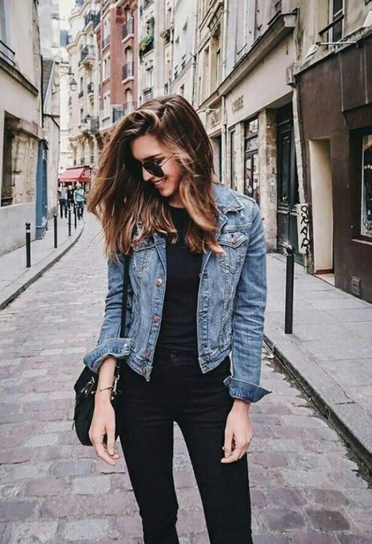 Mulher de pele clara com blusa preta, calça preta e jaqueta jeans