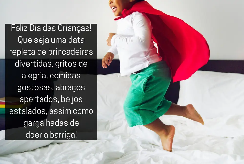Foto de criançça de pele negra usando blusa branca, shorts verde e capa vermelha, pulando na cama, e frase "Feliz Dia das Crianças! Que seja uma data repleta de brincadeiras divertidas, gritos de alegria, comidas gostosas, abraços apertados, beijos estalados, assim como gargalhadas de doer a barriga!"
