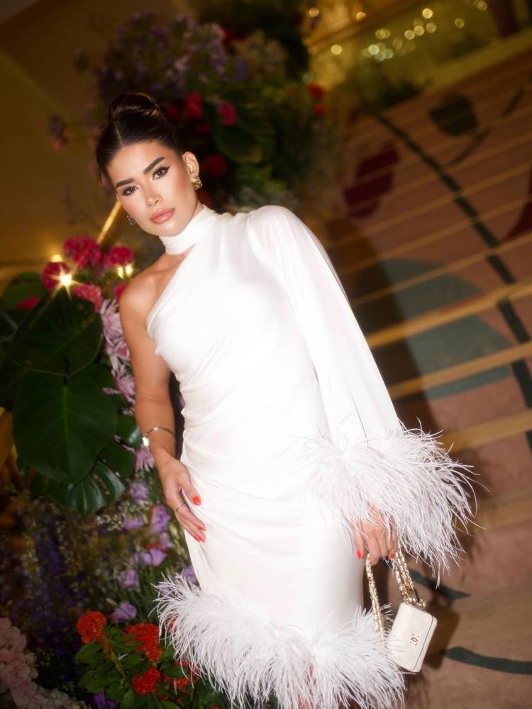 Mulher de pele clara usando vestido branco com plumas, de um ombro só e manga longa.