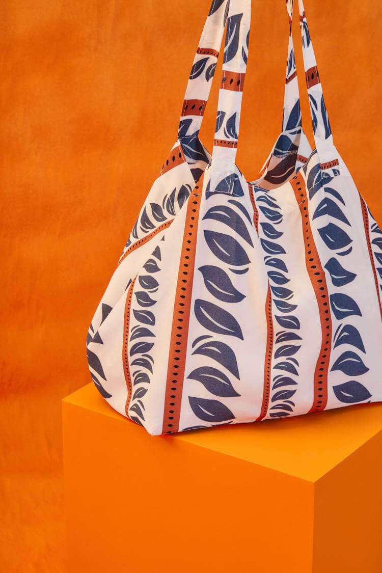 ecobag da Maria Filó branca com estampa de folhas azuis e listras laranjas ecobag da Maria Filó