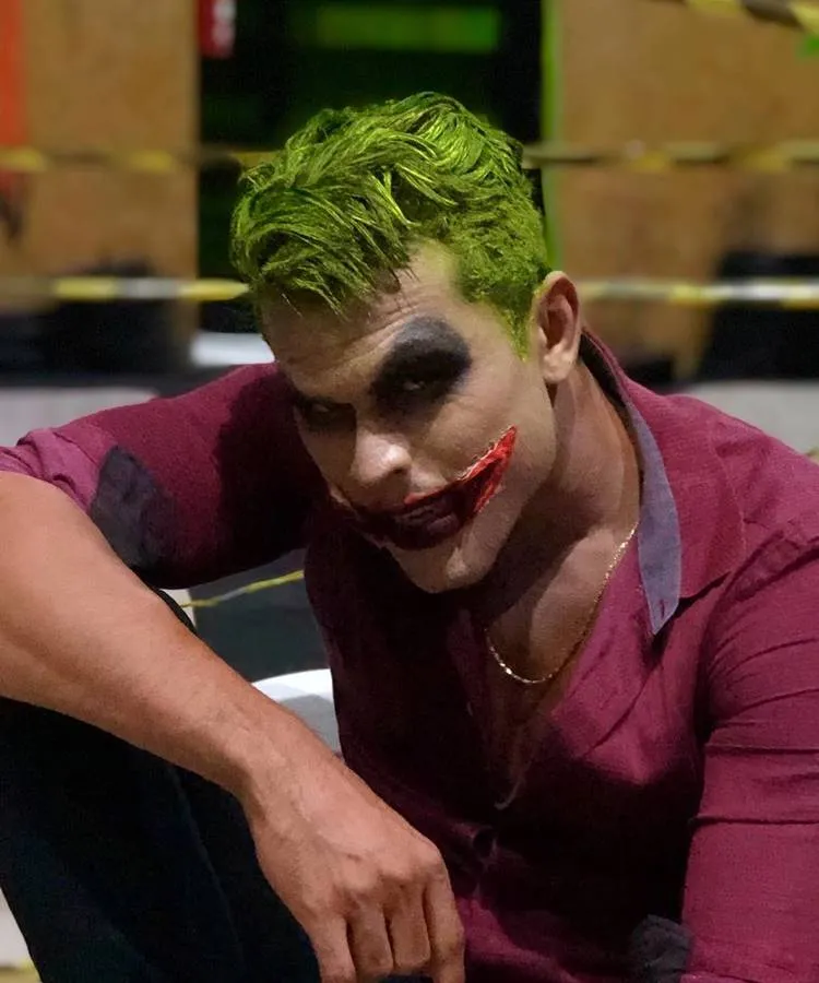 Homem com maquiagem de coringa: cabelo verde, sombra preta, boca vermelha 