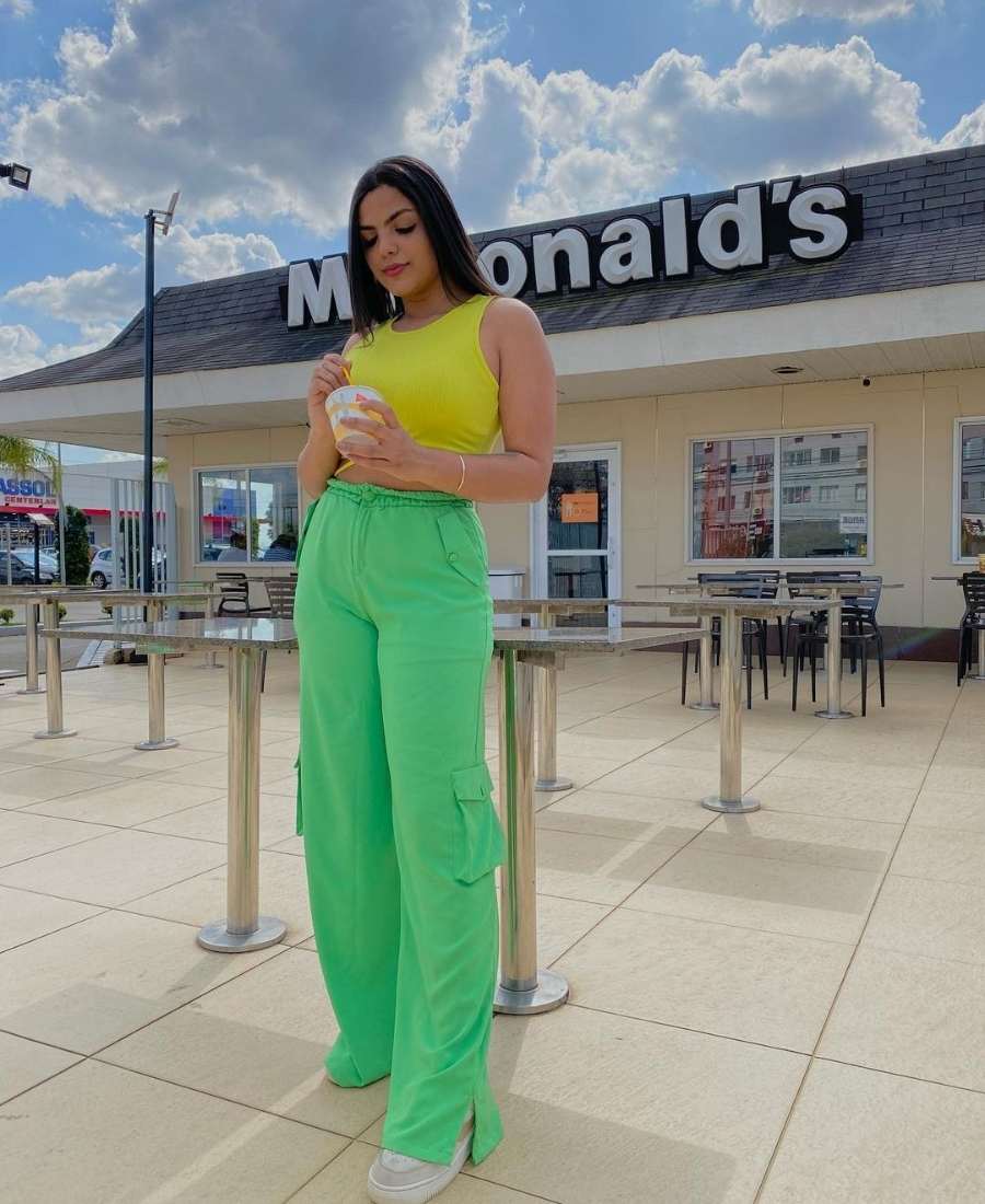 Imagem com fundo de loja do MC Donalds. No centro, mulher usando roupas Brazilcore: camiseta amarela + calça cargo verde.
