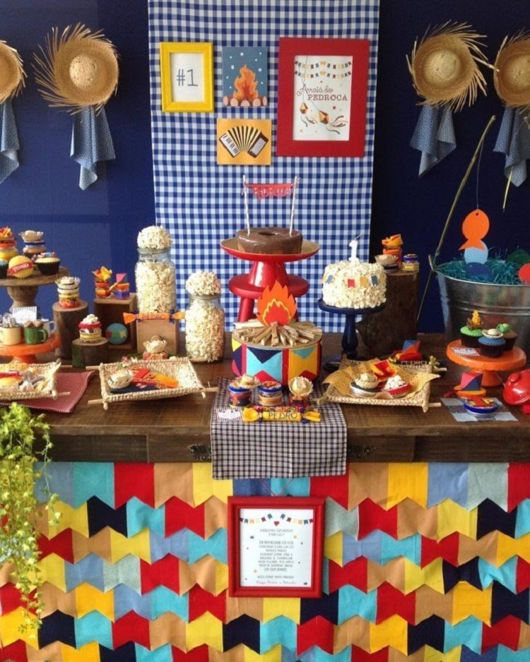 A imagem representa decoração para festa junina. Contém doces e comidas típicas, chapéus de palha, quadros, babado de bandeirinhas