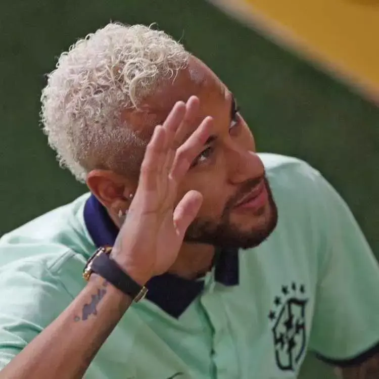Neymar Jr. com camisa polo da seleção brasileira acenando, exibindo relógio e tatuagem escrita no pulso 