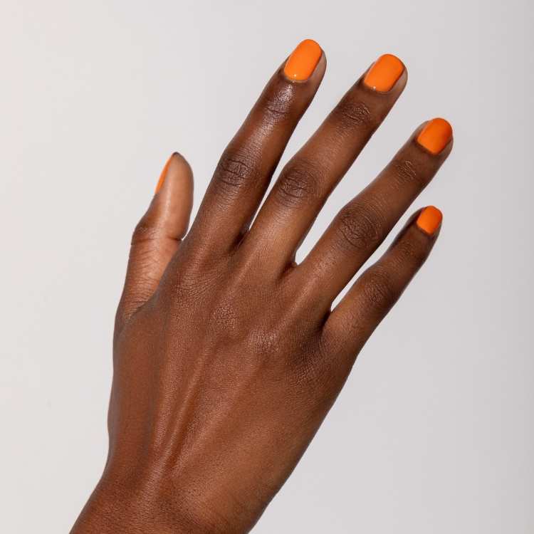 Mão feminina com unhas curtas e ovais pintadas de tangerina vibrante, destacando um laranja enérgico e moderno. O fundo branco neutro realça a intensidade da cor, que reflete a tendência ousada e otimista de esmaltes para o ano de 2025.
