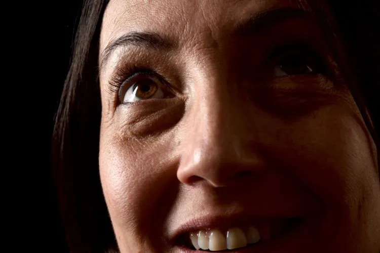 Mulher de idade com a área inferior dos olhos com olheiras. Ela sorri e olha para cima