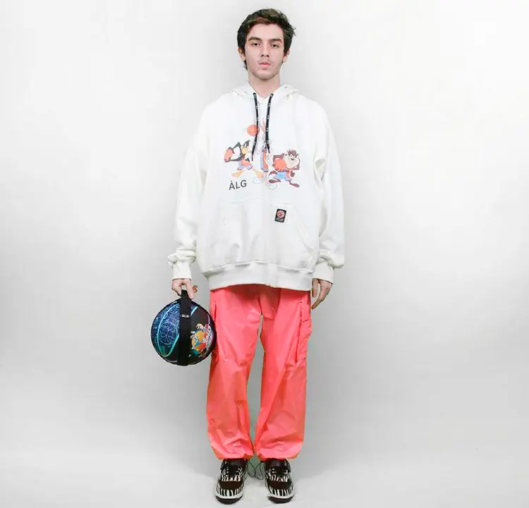 Modelo com moletom branco e calça larga rosa. Ele segura uma bola de basquete azul
